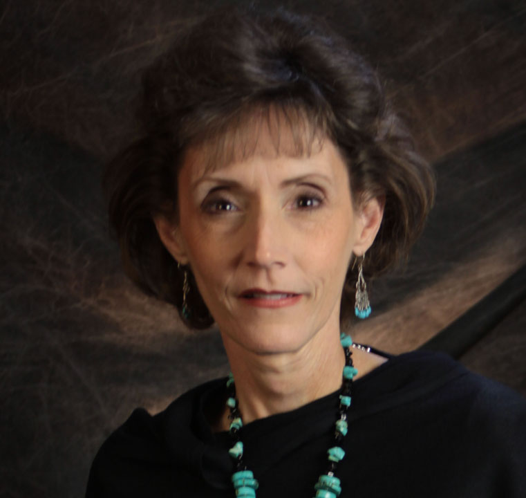 Portrait of a woman with dark hair and turquoise jewelry against a dark backdrop.